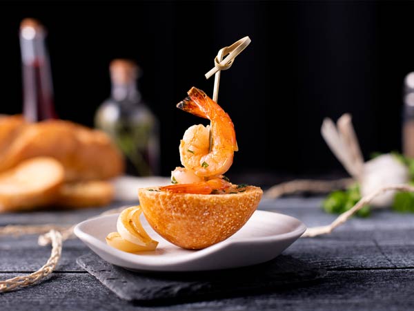 Shrimp cocktail skewer balanced on an orange half-shell with lemon wedges on a white plate